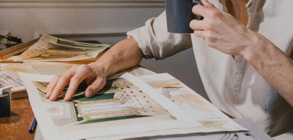 Architect reviews designs at desk, drinking coffee. Indoor creative workspace.